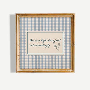 May include: A square wooden frame containing a light blue and white gingham patterned background. Centered is a cream-coloured rectangular card with a scalloped edge, featuring the dark blue text: this is a high class joint act accordingly.