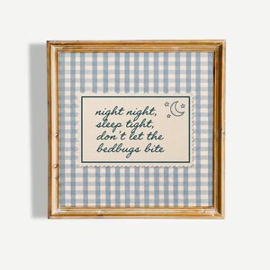 May include: A square framed wall art piece featuring a light blue and white gingham background. Centered is a cream-colored rectangular card with scalloped edges, displaying the dark blue text: night night, sleep tight, don't let the bedbugs bite.