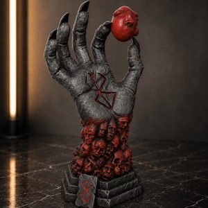 May include: A gray, textured sculpture of a large hand with long, sharp black fingernails, holding a small red egg-shaped object. The wrist area is composed of a cluster of red human faces, and a red symbol is etched into the palm and base.