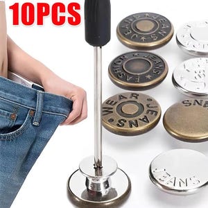 May include: A set of 10 metal replacement buttons for denim jeans, featuring various bronze and silver finishes with embossed text. The set includes a small metal tool with a black handle for installation, shown alongside blue denim fabric.
