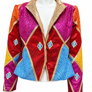 Pode incluir: Um blazer de manga comprida coberto de lantejoulas multicoloridas com um padrão geométrico de losangos em vermelho, magenta, azul, laranja e amarelo. A peça tem uma lapela de lantejoulas douradas e pequenos detalhes em forma de losango azul e branco.