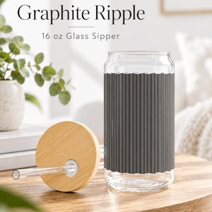May include: A 473 ml glass sipper featuring a dark grey, vertically ribbed silicone sleeve. The set includes a round, light-coloured bamboo lid with a central hole and a clear glass straw. The text Graphite Ripple 16 oz Glass Sipper is visible.