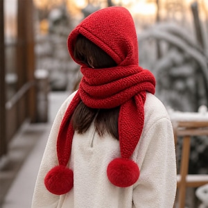 Peut inclure: Une écharpe à capuche rouge vif fabriquée dans une matière texturée semblable à de la polaire. Le modèle comprend une capuche profonde qui se prolonge par une longue écharpe enveloppante avec deux extrémités terminées par un gros pompon rouge.
