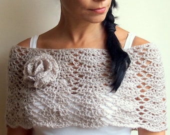 May include: A woman wearing a beige crochet shawl with a flower detail. The shawl is draped over her shoulders and has a delicate, lacy pattern.