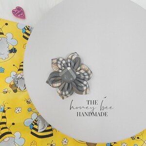 May include: A grey and beige plaid fabric flower hair bow with a silver centre. The bow is on a white background with the text "THE honey bee HANDMADE".