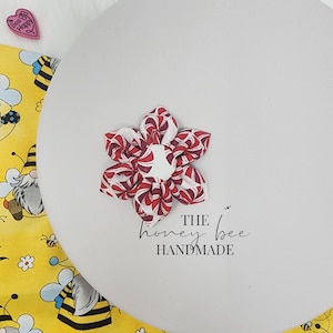 May include: A red and white fabric flower with a swirl pattern. The flower is handmade and has the text "THE honey bee HANDMADE" below it.