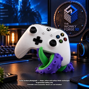 May include: A white video game controller resting on a purple and green octopus tentacle stand. The stand features textured suction cups along the purple exterior and a smooth green interior. The controller has black joysticks and buttons.