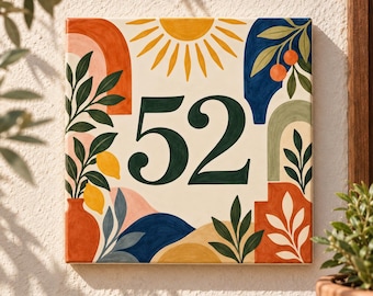 May include: A square house number plaque featuring the number 52 in dark green serif font. The design includes a yellow sun, orange arches, blue shapes, and botanical illustrations of lemons and oranges on a cream background with painted details.