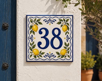 May include: A square ceramic house number tile featuring the number 38 in dark blue. The design includes a hand-painted border with yellow lemons, green leaves, and white blossoms on a cream background, framed by a wavy blue line pattern.