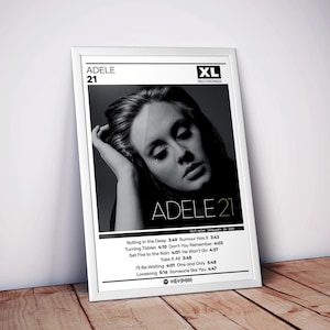 May include: A framed poster featuring the black and white album cover for Adele's 21. The design includes the artist name, album title, XL Recordings logo, and a tracklist with song durations. The text includes Rolling in the Deep, Rumour Has It, Turning Tables, Don't You Remember, Set Fire to the Rain, He Won't Go, Take It All, I'll Be Waiting, One and Only, Lovesong, and Someone like You.