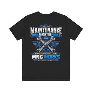 May include: A black t-shirt featuring a graphic design with two crossed silver wrenches over a blue gear. The text reads: MAINTENANCE MAKES PRODUCTION POSSIBLE, REPAIRS, TROUBLESHOOTING, UPTIME, MNC WORKS, and REAL PEOPLE. REAL WORK. in white and blue.