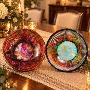 May include: Two circular glass bowls with ribbed edges. The left bowl features a deep red, purple, and black marbled center. The right bowl displays a bright turquoise, yellow, and green marbled center. Both bowls have a reflective, metallic finish.