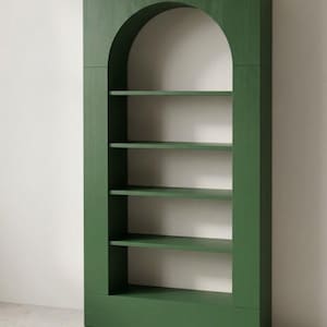 May include: A tall, forest green wooden bookcase featuring a prominent arched top design. The unit includes four horizontal shelves set within a rectangular frame, showcasing a visible wood grain texture throughout the entire structure.