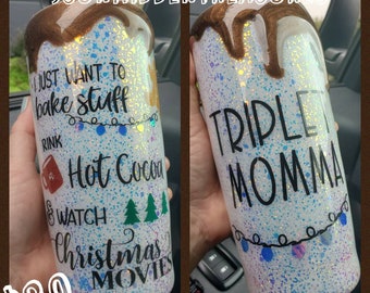 May include: A white glitter tumbler with a brown and white swirl design. The tumbler has the text "I just want to bake stuff" and "Hot Cocoa & Watch Christmas Movies" on one side and "Triple Momma" on the other side.