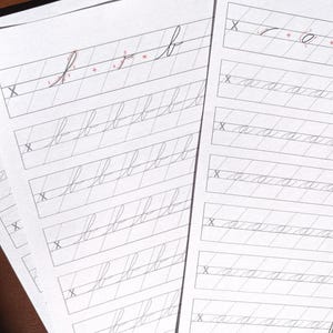 May include: Two white sheets of paper featuring cursive handwriting practice exercises. The left sheet displays rows of the lowercase letter b, while the right sheet shows rows of the lowercase letter a. Each row begins with a grey X.