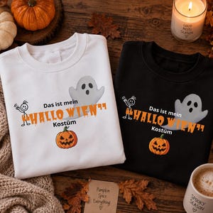 Könnte beinhalten: Ein weißes Sweatshirt und ein schwarzes Sweatshirt, jeweils mit einer Grafik eines Geistes, eines Strichmännchens und eines Kürbisses. Der Text "Das ist mein HALLO WIEN Kostüm" ist in schwarzer und oranger Schrift auf der Brust abgebildet.