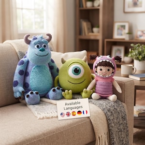 May include: Three crocheted plush toys featuring a large blue monster with purple spots and horns, a round green one-eyed monster, and a small doll wearing a purple monster costume with pigtails. A white card displays the text Available Languages.