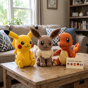 May include: Three handmade crochet plush toys featuring yellow Pikachu, brown Eevee with a fluffy white collar, and orange Charmander with a flame-tipped tail. A small sign sits in front with the text Available Languages: followed by five flag icons.