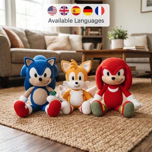 May include: Three crocheted plush toys featuring Sonic the Hedgehog in blue, Tails in yellow, and Knuckles in red. Each character has a beige face, white accents, and stitched details. Sonic holds a small green gem, while all three sit upright.