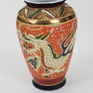 May include: A small, orange and white ceramic vase with a gold rim and a dragon design. The vase is decorated with intricate details and has a black base.