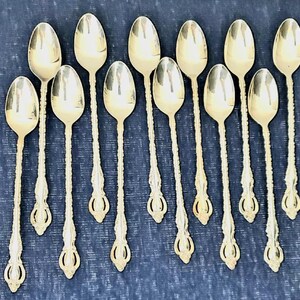 May include: A collection of silver spoons with ornate, twisted handles and oval bowls. The spoons are arranged on a dark blue surface, showcasing their reflective qualities and intricate design. A set of elegant silverware.