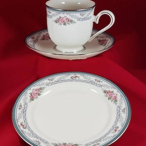 May include: A white teacup and saucer set with a floral design. The cup has a gold rim and a delicate floral pattern with pink roses and green leaves. The saucer has a matching floral design and a gold rim.