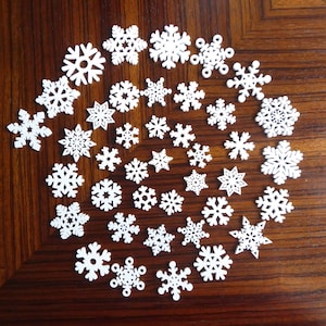 May include: A collection of white snowflake cutouts arranged in a spiral pattern on a brown wooden surface.