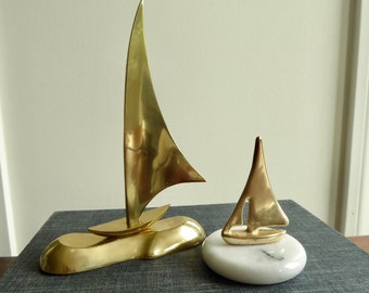 Two brass sailboat sculptures, one with a white stone base