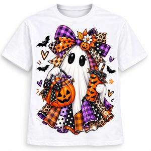May include: A white short-sleeve t-shirt featuring a graphic of a ghost wearing a large bow with leopard and plaid patterns. The ghost holds a jack-o'-lantern candy bucket and an orange cup with bats, surrounded by small bats and hearts.