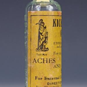 May include: A vintage glass bottle with a yellow label that reads "Kickapoo Indian Medicine Ether Oil In External Use For the Aches and Pains" and "Price 30 Cents".