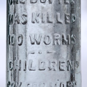 May include: A vintage glass bottle with embossed text. The bottle reads "Bumsted's Worm Syrup" and other text including "One bottle has killed 100 worms". The bottle is clear with a slight blue tint.