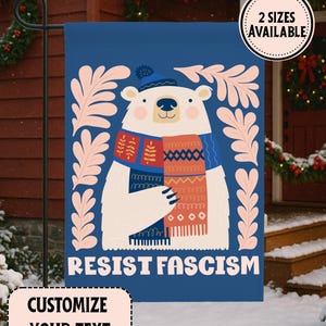 Peut inclure: Un drapeau de jardin bleu avec un ours polaire de dessin animé portant un chapeau et une écharpe, avec les mots "RESIST FASCISM". Le drapeau a une bordure blanche et le texte "PERSONNALISEZ VOTRE TEXTE" en bas. Deux tailles sont disponibles.
