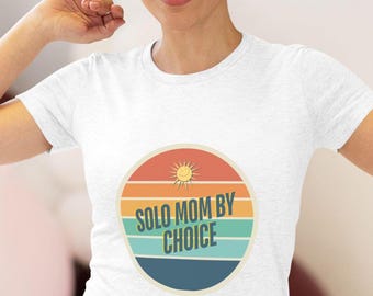 May include: White t-shirt with a retro-style sun graphic and the text "Solo Mom By Choice".