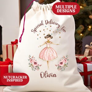 May include: A cream-colored drawstring gift bag with a ballerina design. The bag features the text "Special Delivery For" and the name "Olivia". The design includes a ballerina, stars, and floral accents. The bag is surrounded by wrapped gifts.