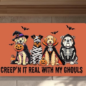 Op de afbeelding: Oranje Halloween deurmat met vier honden in kostuums: een heks, een mummie, een vampier en een skelet. De tekst "Creep'n It Real With My Ghouls" staat onderaan, met vleermuizen.