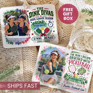 May include: Two rectangular white ornaments featuring pickleball themes. One displays two people with the text THE DINK DIVAS 2026 LEAGUE SEASON 12 WINS 3RD PLACE JENNA + SARAH. The other shows one person with THE YEAR I BECAME OBSESSED WITH PICKLEBALL JENNA 2026 BOULDER PICKLEBALL CLUB.