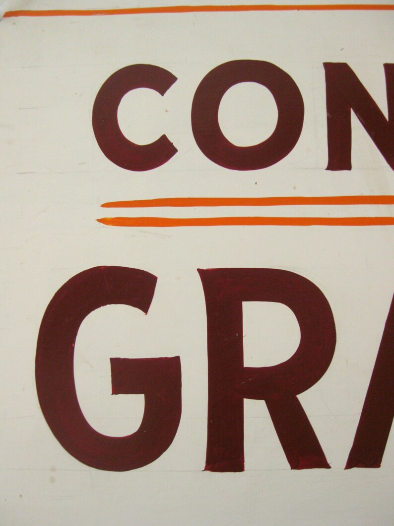 May include: Close-up of a white surface with the word "CON" in large, dark red letters. Below, the word "GRA" is also visible in the same color. Two orange horizontal lines are above and below the word "CON".