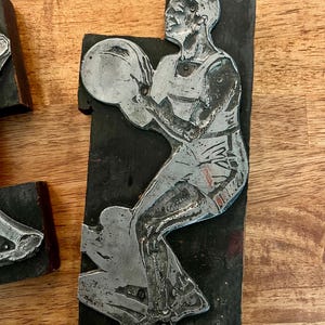 Peut inclure: Bloc d'impression en m&eacute;tal vintage repr&eacute;sentant un joueur de basket-ball en action. La figurine argent&eacute;e est mont&eacute;e sur un bloc de bois noir rectangulaire. Le joueur tient un ballon de basket. Le bois est vieilli.