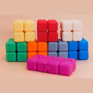 Puede incluir: Una colección de siete juguetes antiestrés tipo cubo infinito multicolor dispuestos en grupo. Los cubos son amarillos, rojos, blancos, verdes, naranjas, grises, azules y magenta. Cada juguete consta de ocho bloques conectados.