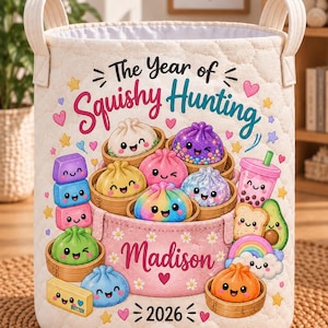 May include: A cream-colored quilted fabric storage basket featuring the text The Year of Squishy Hunting, Madison, and 2026. The design includes colorful cartoon illustrations of various smiling dumplings in bamboo steamers, boba tea, and butter.