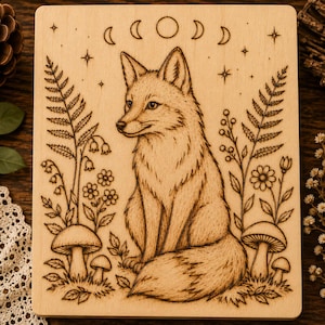 May include: A rectangular light-colored wooden plaque featuring a pyrography illustration of a fox sitting centrally. The fox is surrounded by ferns, small flowers, and mushrooms. Above the fox are moon phases and stars etched into the wood.