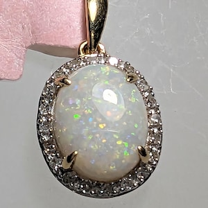 Op de afbeelding: Een gouden hanger met een witte opaal omringd door een halo van kleine diamanten.