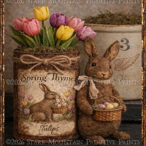 May include: A rustic Easter-themed still life. A brown rabbit figurine holds a basket of eggs next to a tin can vase filled with tulips. The vase is decorated with a rabbit illustration and the words "Spring Thyme" and "Tulips". A vintage crock is in the background.