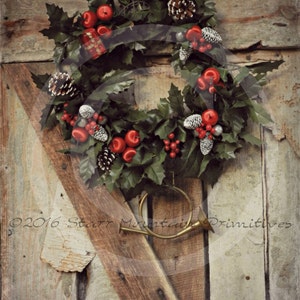 Op de afbeelding: Een rustieke houten deur met een kerstkrans van hulst, rode bessen en dennenappels. Een hoorn van messing hangt aan de deur, en de tekst "Peace On Earth" staat onder de krans.
