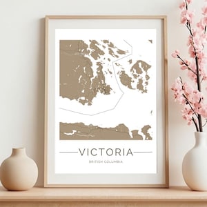 May include: A framed print of a map of Victoria, British Columbia. The map is in a light brown color and shows the city's coastline and surrounding islands. The text "VICTORIA" and "BRITISH COLUMBIA" is printed below the map.