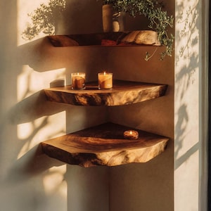 May include: Three tiered corner shelves made of dark brown natural wood with live edges. The top shelf holds a ceramic pot with a green plant. The middle shelf holds two lit glass candles. The bottom shelf holds one small lit glass candle.