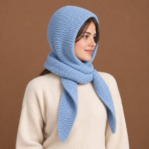 May include: A light blue knitted hood scarf with a textured, moss-like stitch pattern. The accessory features a rounded hood section that transitions into two long, pointed ends that drape down the front, crafted from soft yarn material.