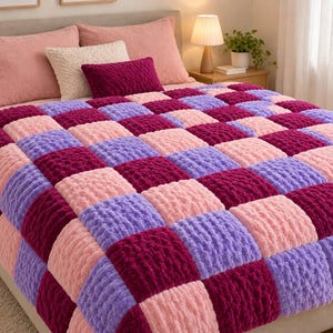 May include: A plush, chunky knit blanket featuring a chequered pattern of alternating squares in shades of deep magenta, light lavender, and soft pastel pink. The blanket has a thick, textured, yarn-based construction with a soft, fuzzy appearance.