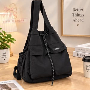May include: A black canvas backpack featuring two front pockets with flaps, a drawstring closure with a black and white patterned cord, and two shoulder straps. A small rectangular label on the front pocket reads FASHION BAGS.