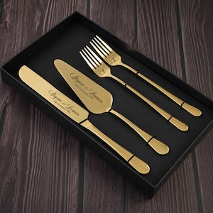 May include: A gold-toned cake serving set consisting of a knife, a cake server, and two forks, all presented in a black box. The knife and server are engraved with the text Alyssa & Logan 04.12.2025, while the two forks feature a small letter L.